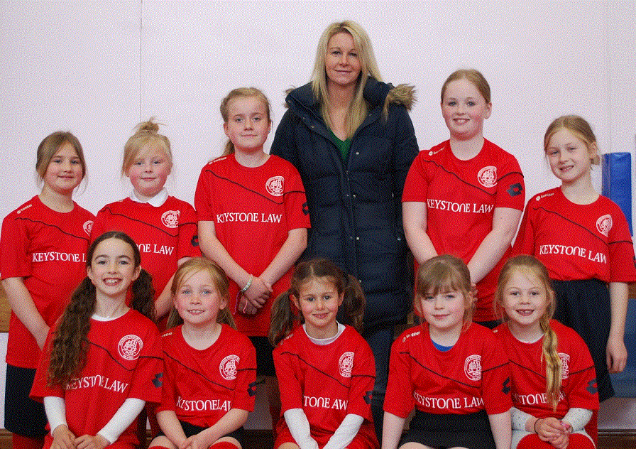Gillian Christian with girls from local football team wearing red kit with Keystone Law logo on the front as sponsor