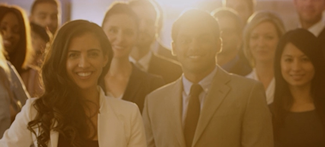 A group of professionals in suits smiling with the sunshine behind them giving an orange glow