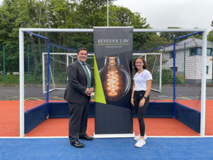 Photo of Sienna Dunn and Keystone Law Isle of Man's William Margot in front of a hockey goal, with the Keystone Law banner between them
