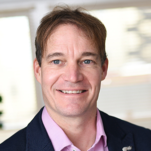 Headshot of Guy Hitchin wearing a pink shirt smiling at the camera