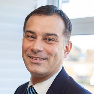 Headshot of Dan Cowley wearing a suit looking to the side of the camera