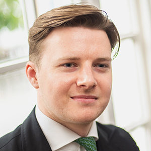 Headshot of Henry Powell in a suit looking next to the camera