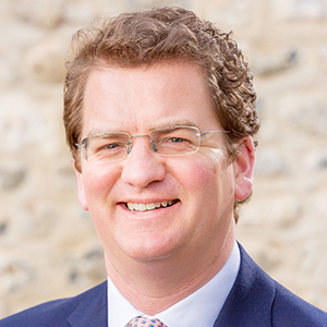 Headshot of Simon Mackie wearing a suit looking into the camera